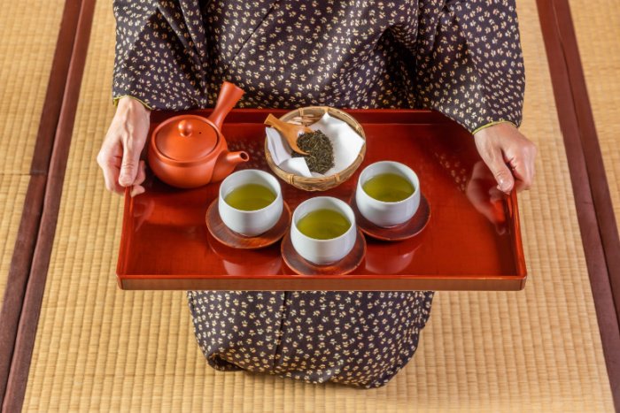 A person in a kimono offers a tray of green tea